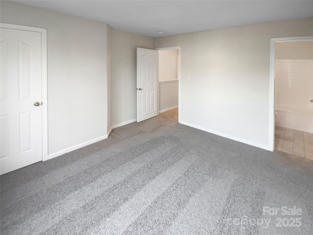 unfurnished bedroom with carpet flooring, baseboards, and ensuite bathroom