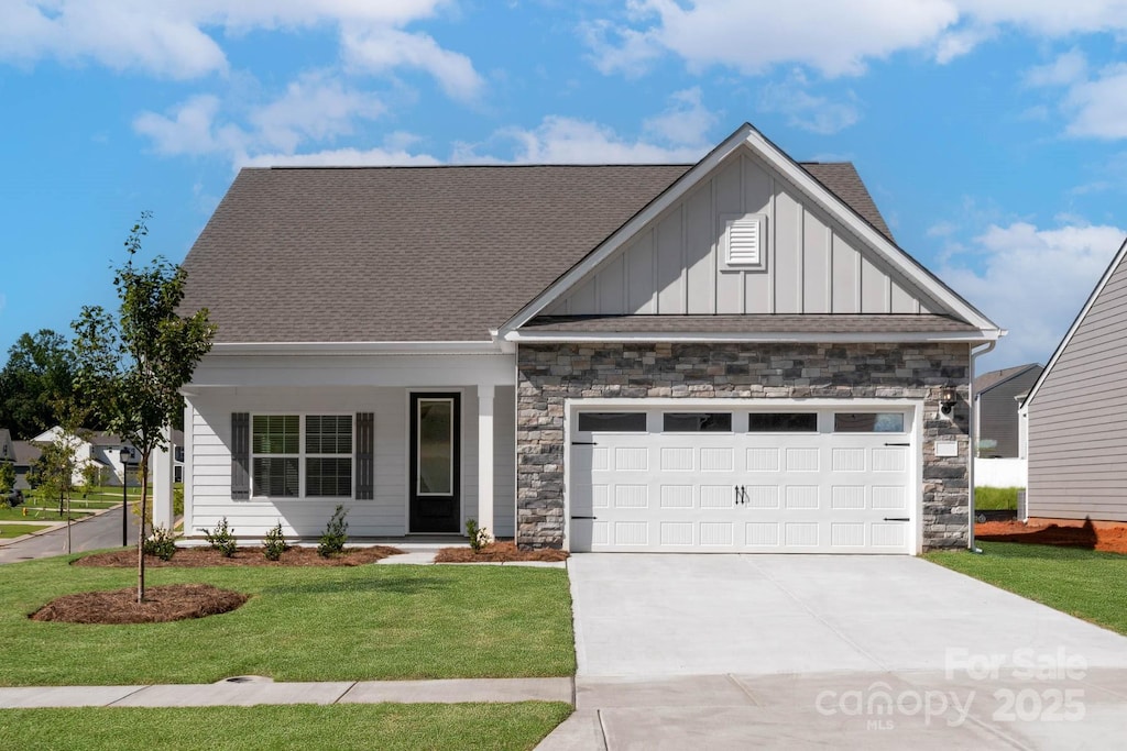 view of front of property with board and batten siding, a front yard, a garage, stone siding, and driveway