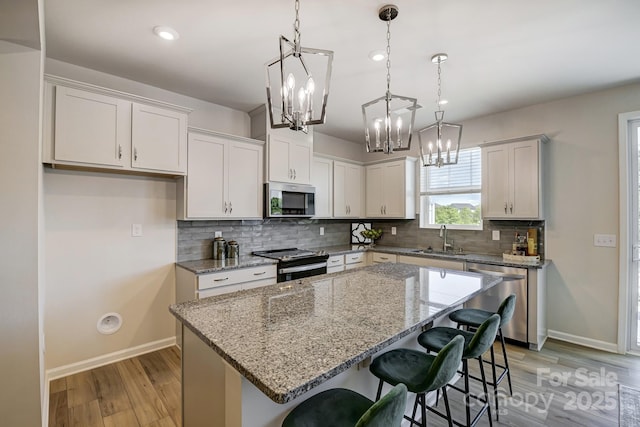 kitchen with a kitchen island, light wood-style flooring, appliances with stainless steel finishes, a notable chandelier, and a sink