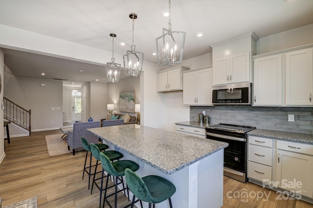 kitchen featuring tasteful backsplash, stainless steel microwave, a kitchen island, electric range oven, and white cabinetry