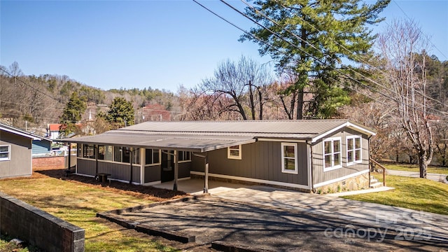 view of front of home featuring driveway, a sunroom, a carport, a front lawn, and metal roof