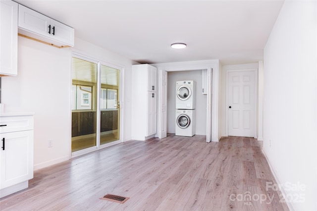 interior space featuring visible vents, baseboards, laundry area, light wood-style floors, and stacked washer / drying machine