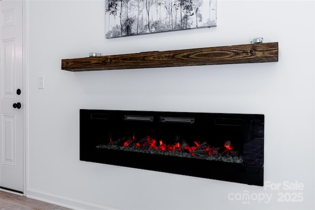 interior details with wood finished floors, baseboards, and a lit fireplace