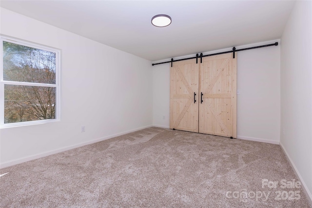 unfurnished bedroom with a barn door, baseboards, and carpet flooring