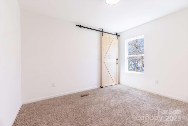 carpeted spare room with a barn door, baseboards, and visible vents