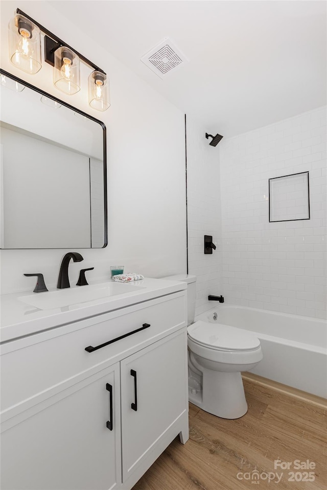 bathroom with visible vents, tub / shower combination, toilet, wood finished floors, and vanity