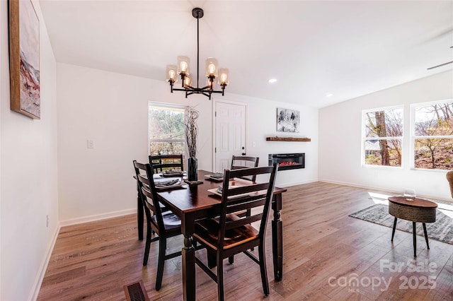 dining space with a glass covered fireplace, a notable chandelier, visible vents, and wood finished floors