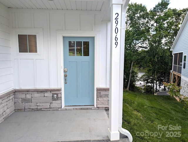 entrance to property featuring board and batten siding, a lawn, and stone siding
