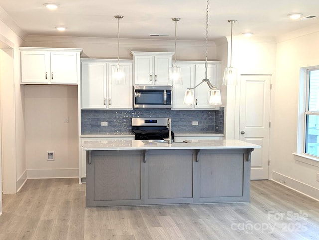 kitchen with appliances with stainless steel finishes, light wood-style floors, light countertops, white cabinetry, and a center island with sink