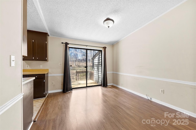 unfurnished dining area featuring light wood-style flooring, ornamental molding, baseboards, and a textured ceiling