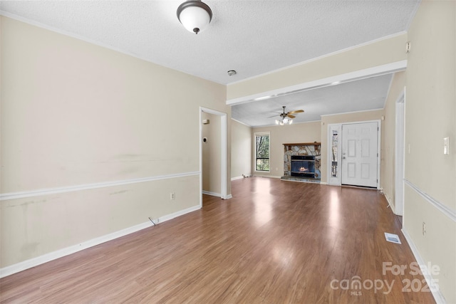 unfurnished living room with a stone fireplace, a ceiling fan, visible vents, and wood finished floors