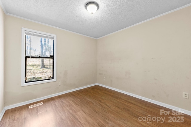 unfurnished room with wood finished floors, visible vents, baseboards, a textured ceiling, and crown molding