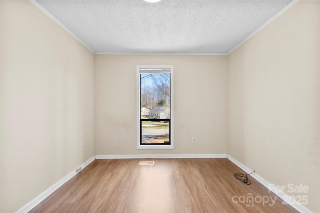 spare room with crown molding, wood finished floors, baseboards, and a textured ceiling