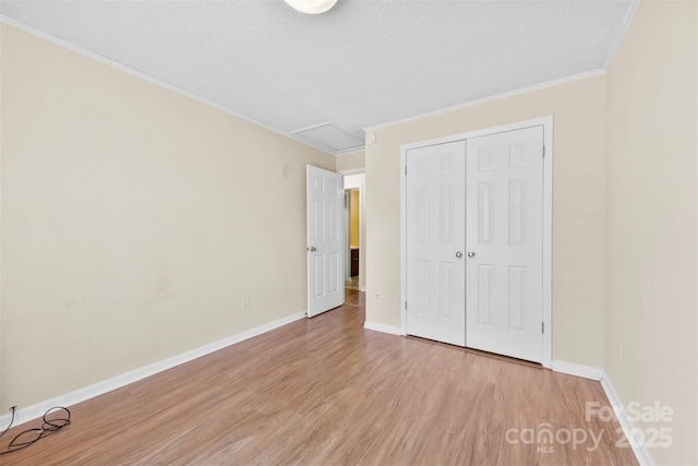 unfurnished bedroom with ornamental molding, a textured ceiling, a closet, light wood finished floors, and baseboards