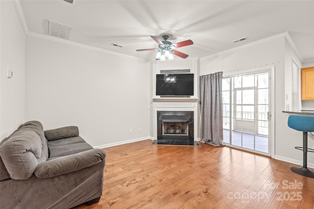 living room with visible vents, crown molding, a tiled fireplace, light wood-type flooring, and a ceiling fan