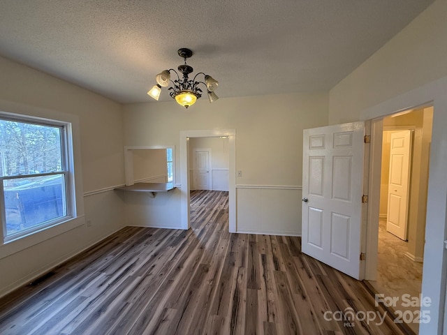 unfurnished dining area featuring visible vents, a textured ceiling, an inviting chandelier, and wood finished floors