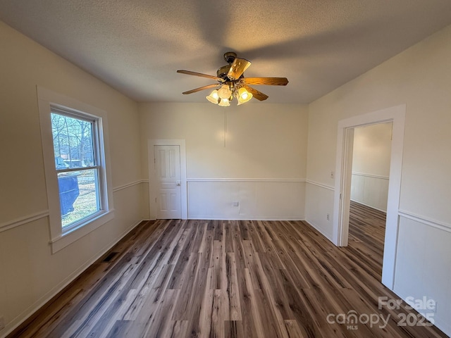 empty room with visible vents, a textured ceiling, a ceiling fan, and wood finished floors