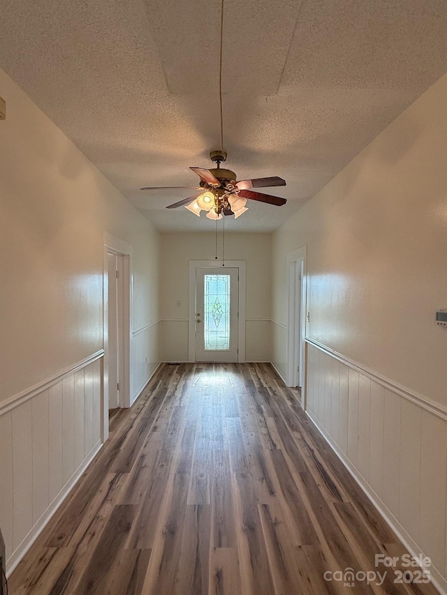 unfurnished room with a wainscoted wall, a textured ceiling, a ceiling fan, and wood finished floors