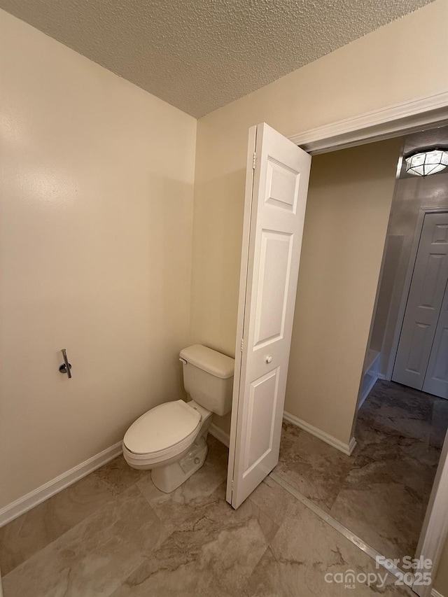 bathroom with a textured ceiling, toilet, and baseboards