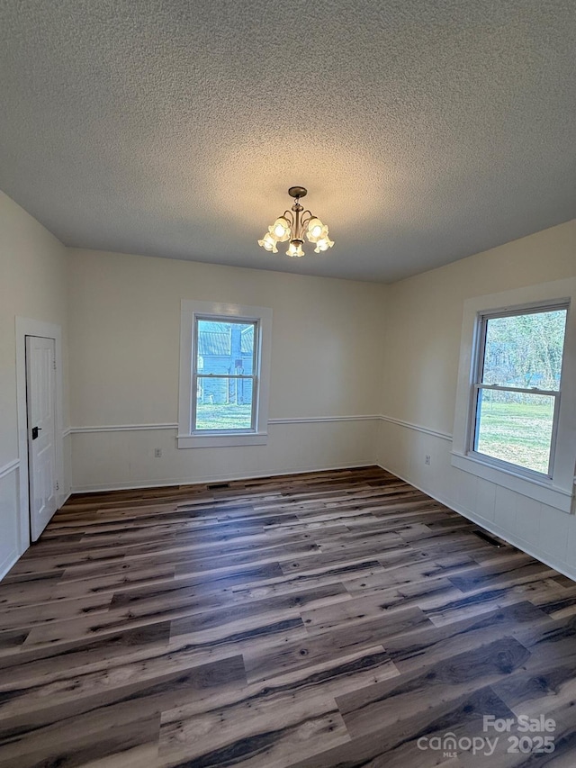 unfurnished room with an inviting chandelier, wood finished floors, and wainscoting