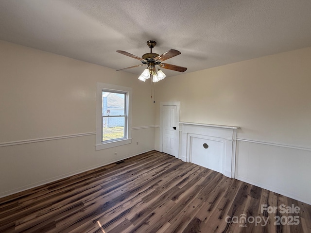 spare room featuring a textured ceiling, dark wood-style floors, a wainscoted wall, and ceiling fan