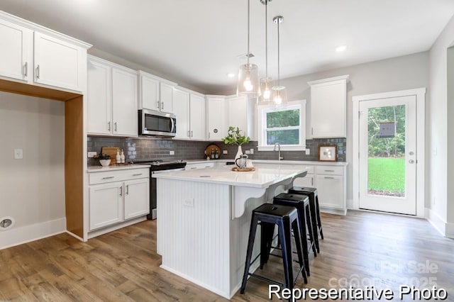 kitchen with a kitchen island, light wood-style flooring, decorative backsplash, white cabinets, and appliances with stainless steel finishes