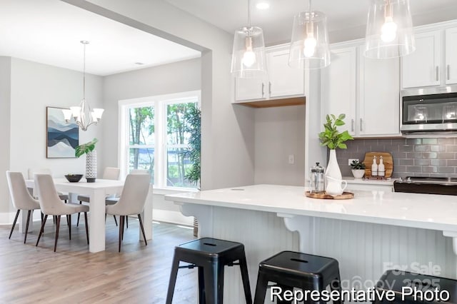 kitchen featuring stainless steel microwave, backsplash, white cabinetry, light wood finished floors, and light countertops