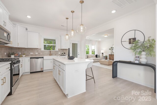 kitchen with a sink, a kitchen breakfast bar, appliances with stainless steel finishes, a kitchen island, and tasteful backsplash