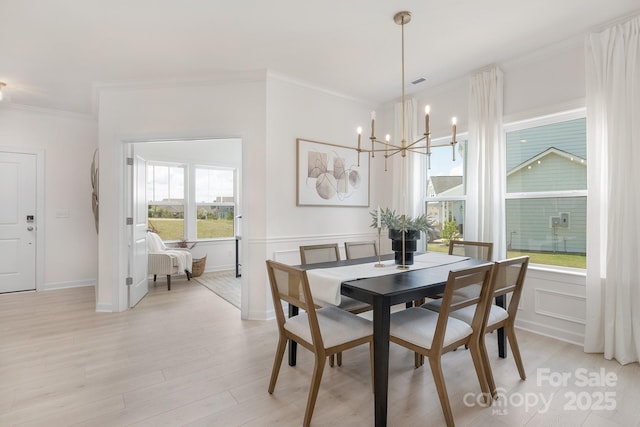 dining space featuring an inviting chandelier, crown molding, light wood-type flooring, visible vents, and wainscoting