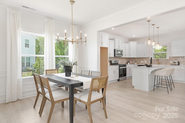 dining room featuring light wood-style floors, visible vents, ornamental molding, and a notable chandelier