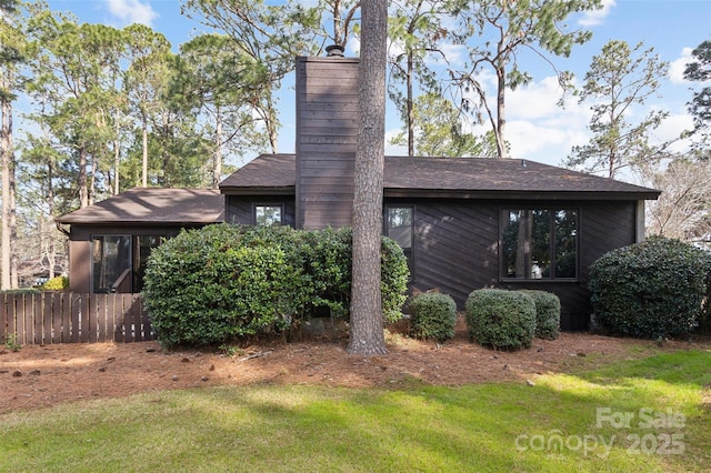 view of home's exterior with a chimney, roof with shingles, a yard, and fence