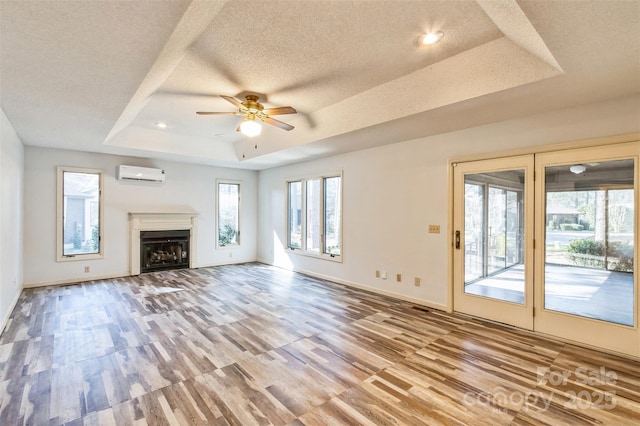 unfurnished living room featuring a ceiling fan, a textured ceiling, wood finished floors, a wall unit AC, and a raised ceiling