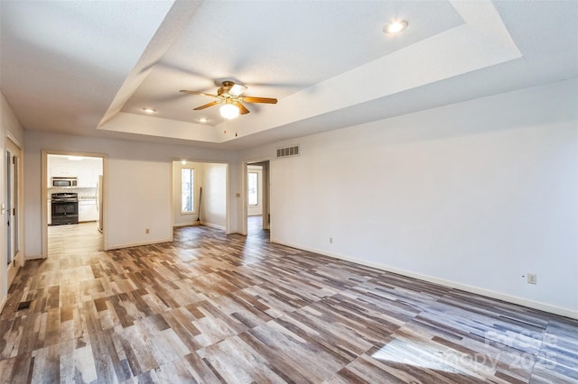 spare room featuring ceiling fan, baseboards, light wood-type flooring, and a tray ceiling