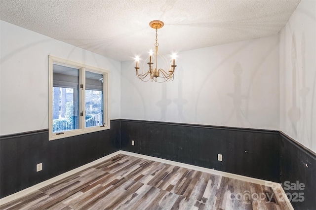 empty room featuring a notable chandelier, a wainscoted wall, a textured ceiling, and wood finished floors