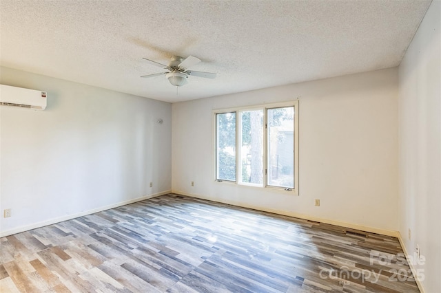 unfurnished room with a wall mounted air conditioner, a textured ceiling, wood finished floors, baseboards, and ceiling fan