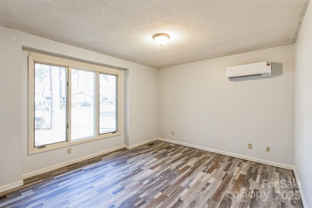 unfurnished room featuring a wall unit AC, wood finished floors, baseboards, and a textured ceiling