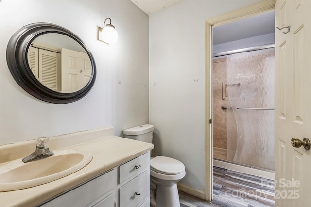 bathroom with toilet, wood finished floors, a shower stall, baseboards, and vanity