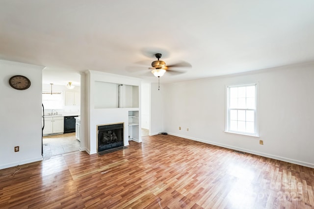 unfurnished living room with a fireplace with flush hearth, a sink, wood finished floors, baseboards, and ceiling fan