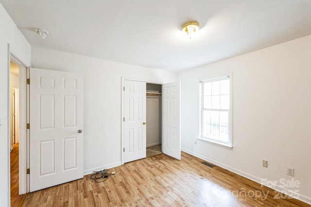 unfurnished bedroom with a closet, visible vents, baseboards, and wood finished floors