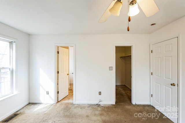 unfurnished bedroom with a walk in closet, visible vents, carpet flooring, baseboards, and ceiling fan