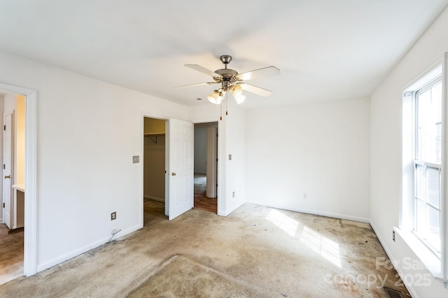 unfurnished bedroom with baseboards, a ceiling fan, a spacious closet, and carpet