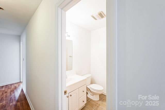 half bath with visible vents, toilet, vanity, and baseboards