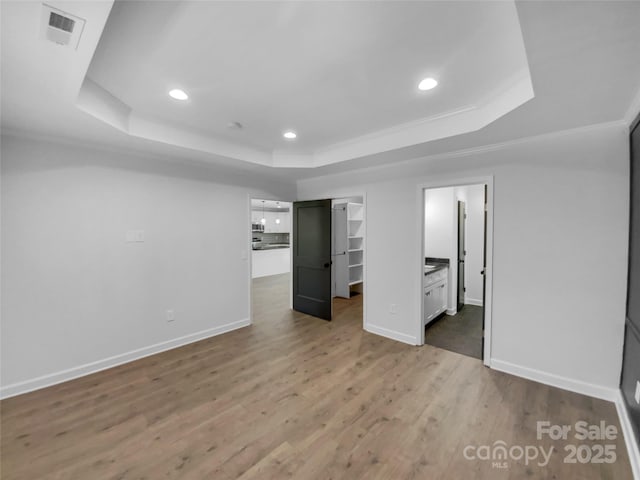 unfurnished bedroom featuring a walk in closet, visible vents, a tray ceiling, wood finished floors, and baseboards