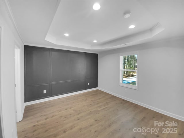 unfurnished room with a raised ceiling, a decorative wall, and wood finished floors