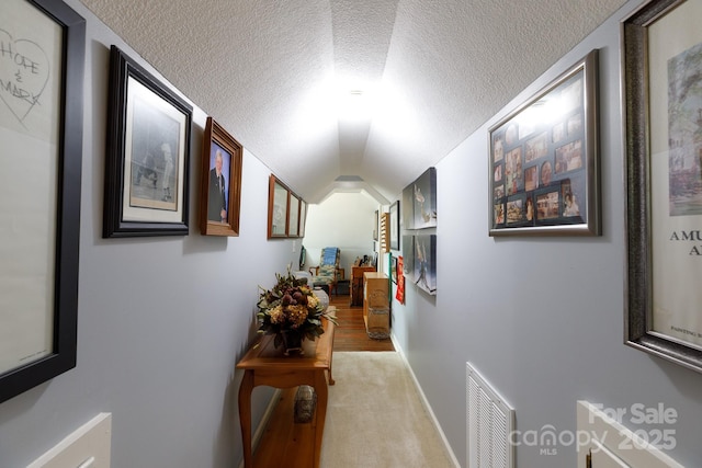 hall featuring vaulted ceiling, light colored carpet, visible vents, and a textured ceiling