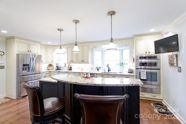 kitchen with a warming drawer, stainless steel appliances, cream cabinetry, and wood finished floors