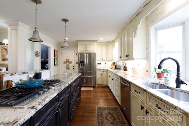 kitchen with dark wood-style flooring, a sink, stainless steel appliances, cream cabinetry, and decorative light fixtures