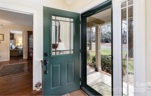 entryway with crown molding, wood finished floors, and baseboards