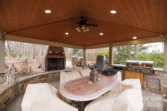 view of patio / terrace featuring a ceiling fan, a gazebo, grilling area, an outdoor stone fireplace, and an outdoor kitchen