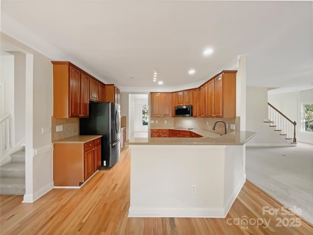 kitchen with light wood finished floors, a peninsula, a sink, light countertops, and appliances with stainless steel finishes